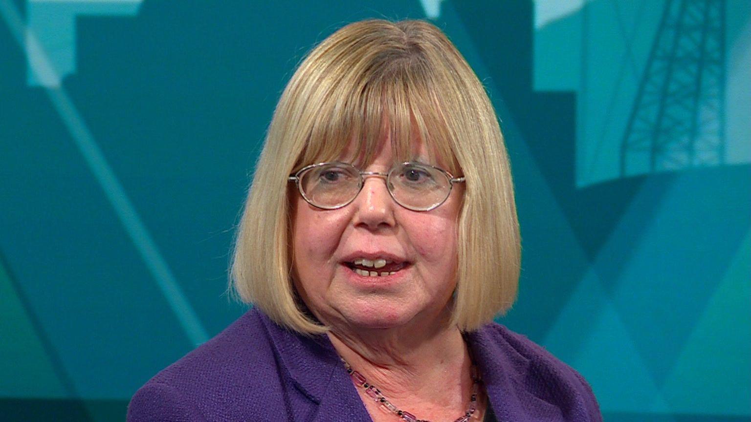 Liz Twist has short blonde hair and is wearing glasses. She is wearing a purple blazer and is sitting in the blue/red Politics North studio.