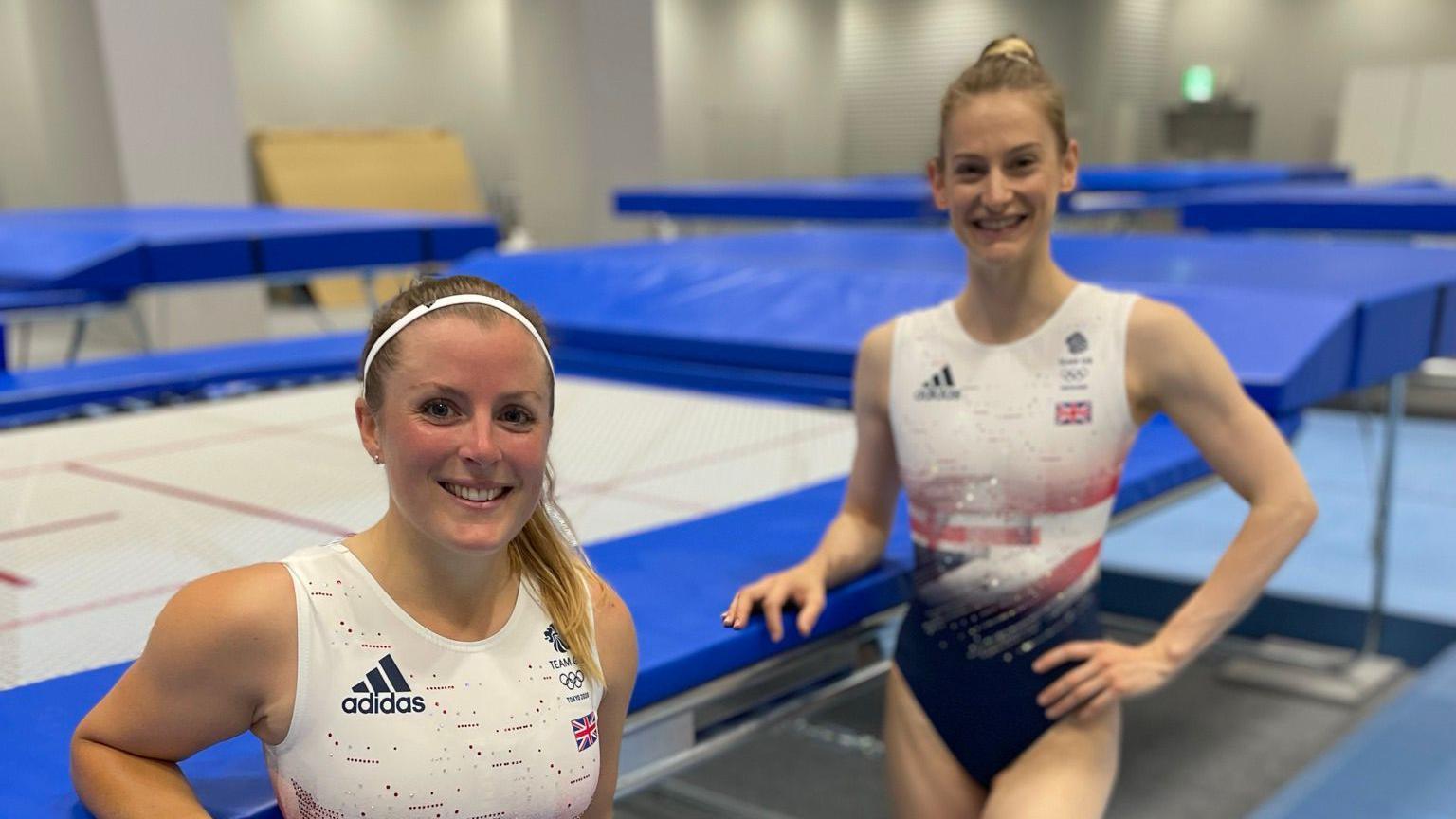 At the bottom left of the photo is Laura from the chest up, wearing a Team GB and a headband. On the right of the photo is Bryony Page in a Team GB leotard and her hair in a bun. Both are leaning  on a trampoline. 