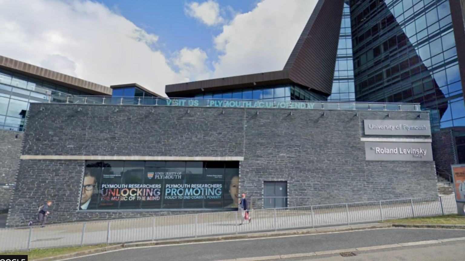 Two people walk in opposite directions past a grey University of Plymouth building 