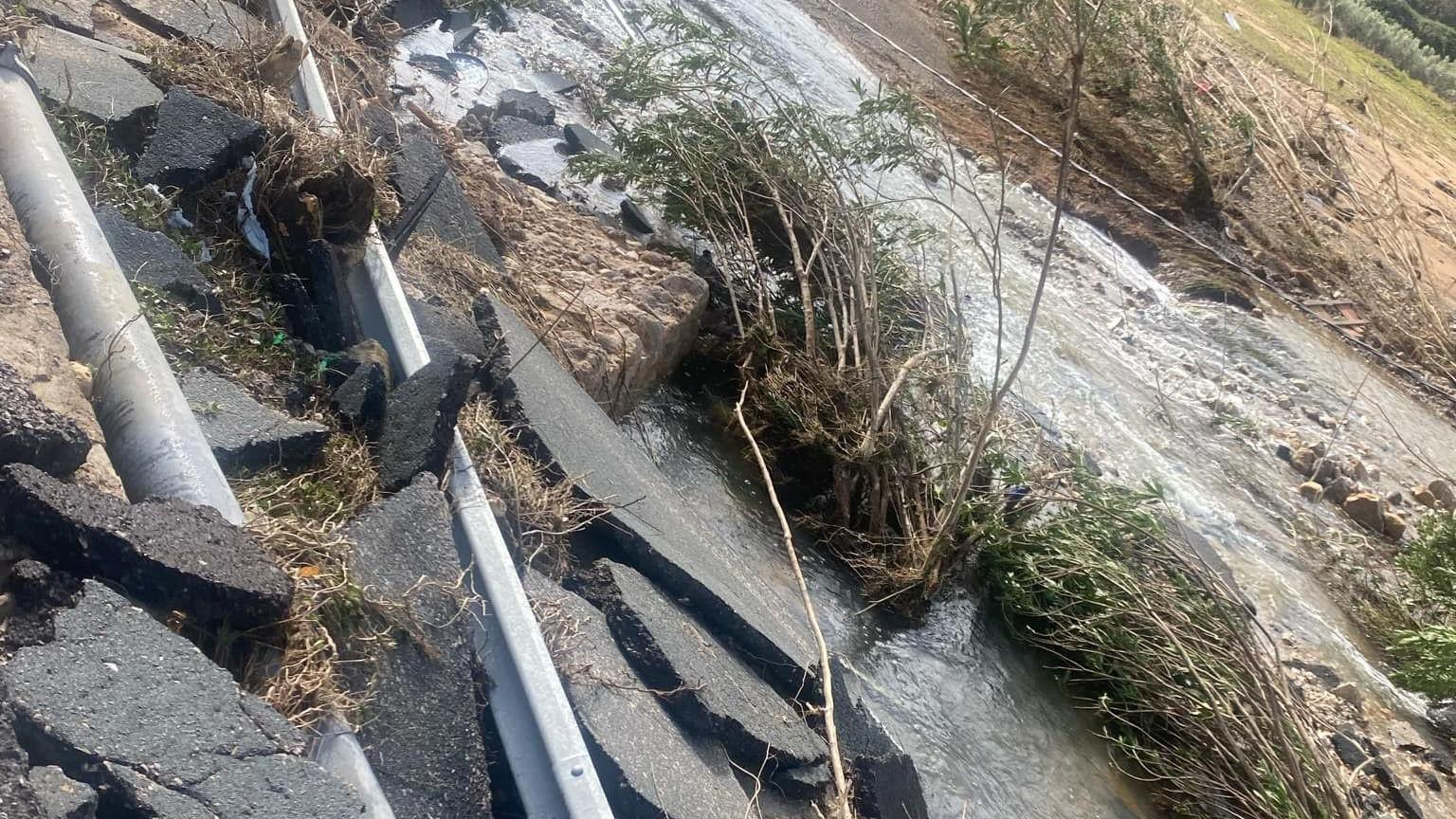 Floodwater pouring down a mountain and parts of a broken road falling down a verge.