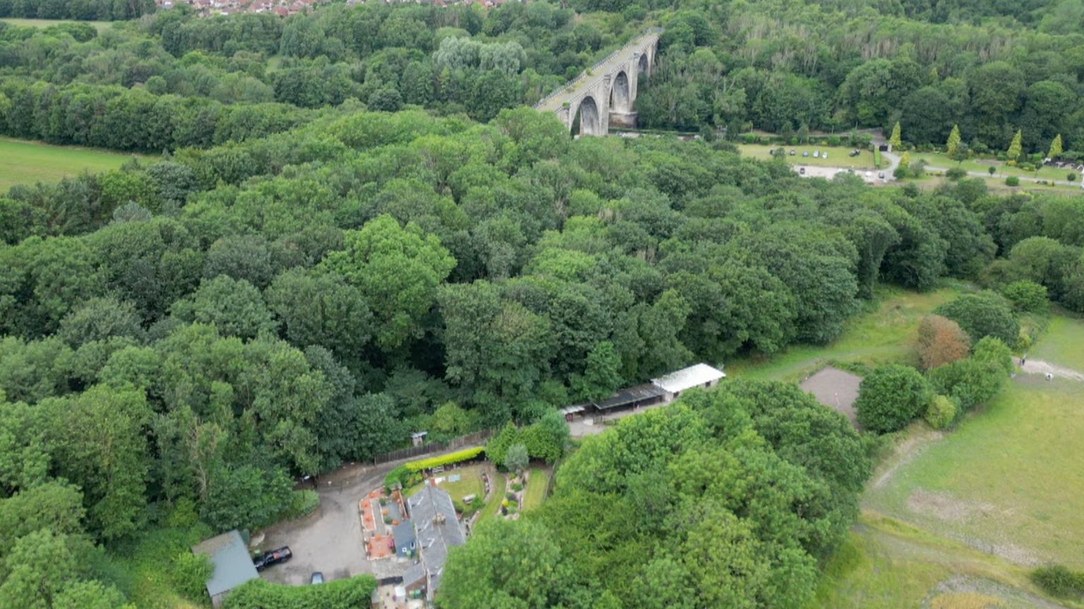 An aerial photograph showing the viaduct in the far distance and Mr Potts' cottage below. It is surrounded by trees which cover the footpaths and roads leading up to the homes.