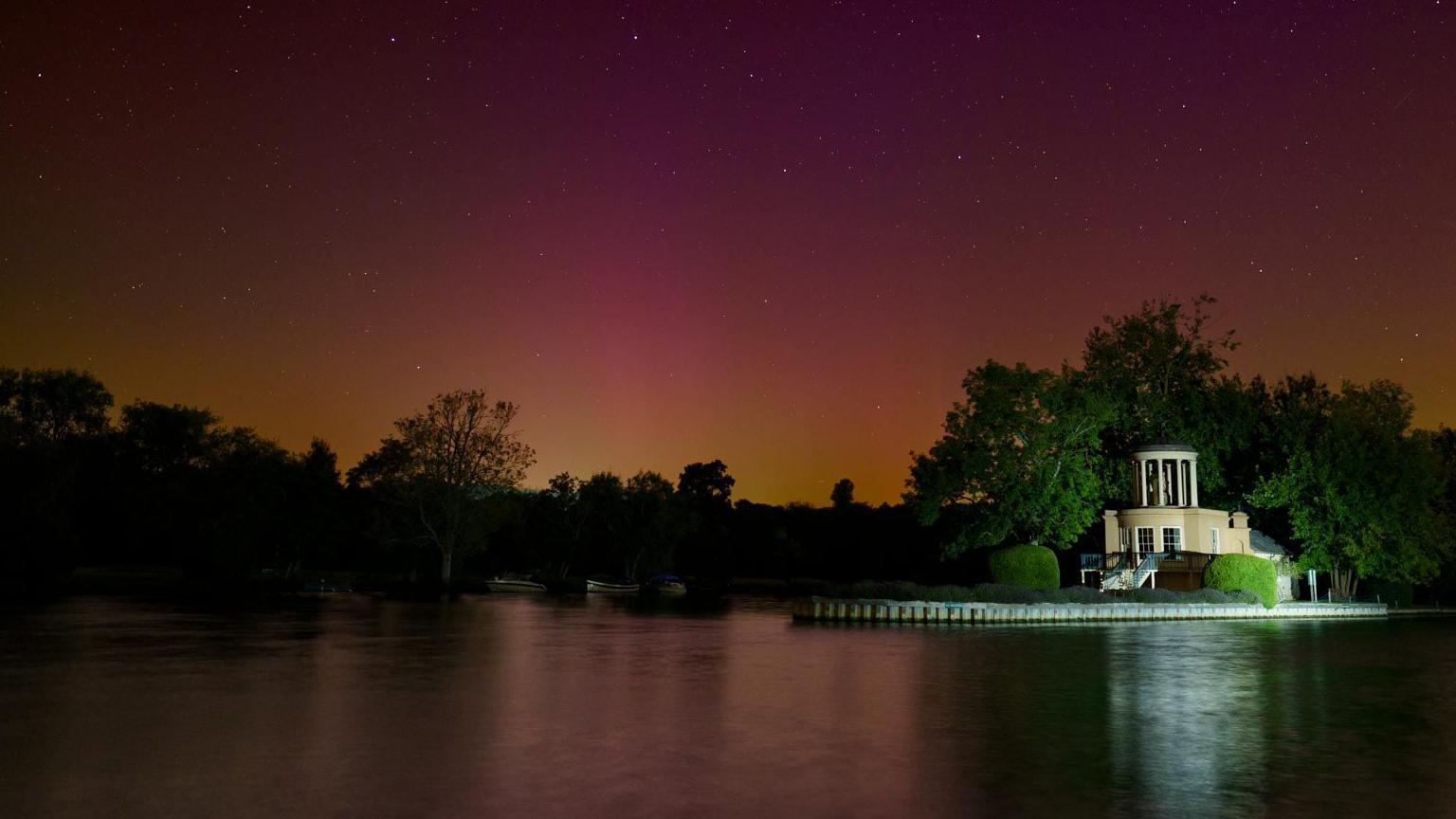 The Northern Lights from Temple Island near Henley. The sky has purple, pink and orange hues which reflect in the water.