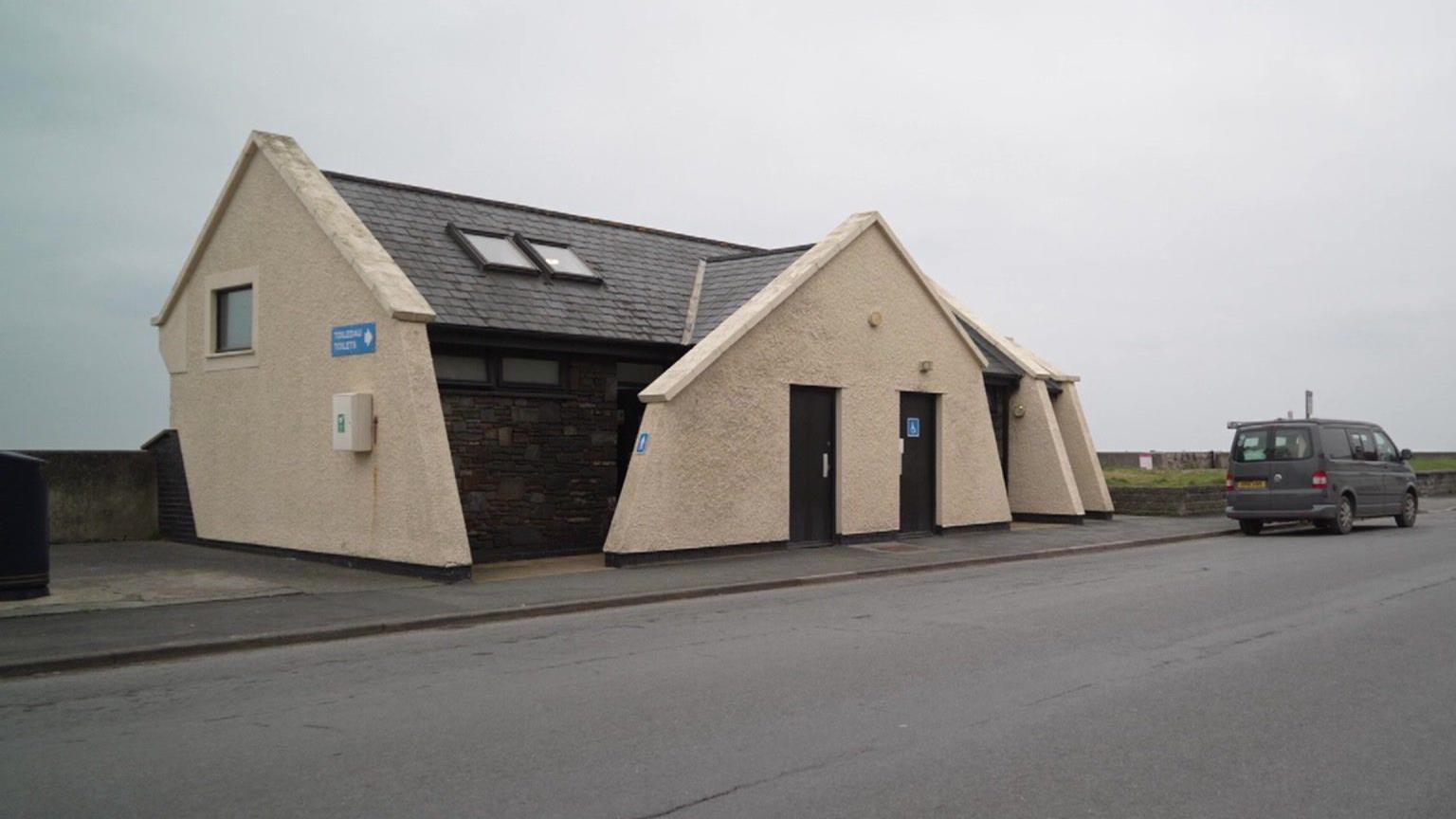 An image of a public toilet block in Ceredigion on a coastline. In the background, there is a beach that is out of sight.