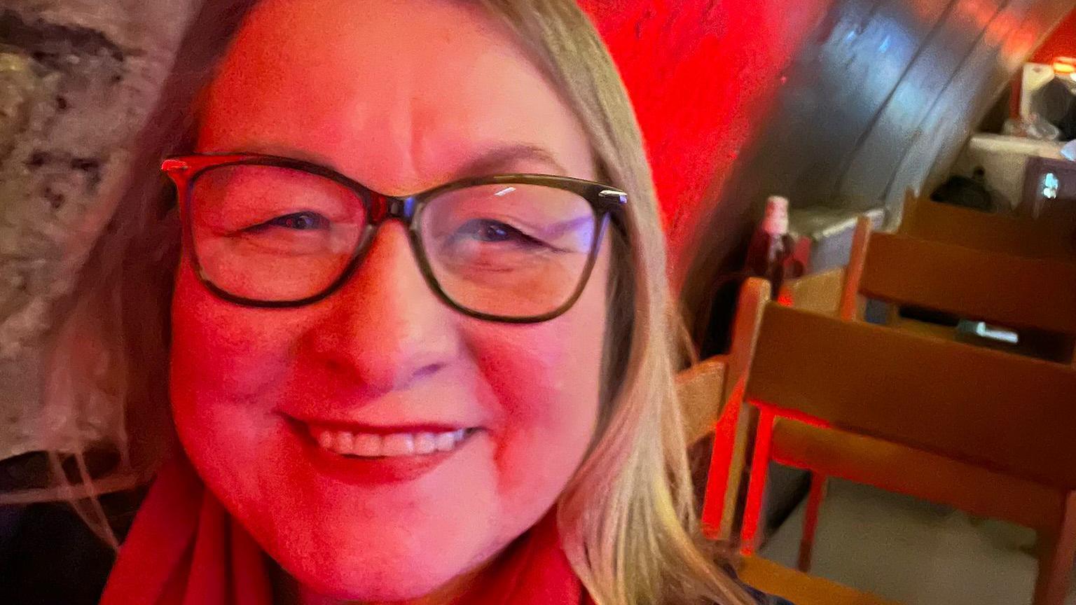 Jan Warren, with long blonde hair and glasses, takes a selfie in a disco setting.