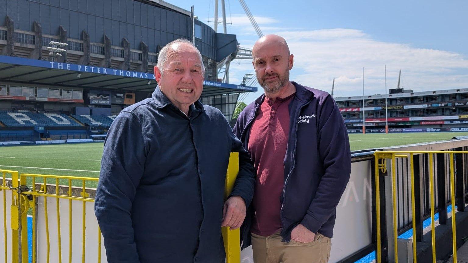 Chris Griffiths a'i fab Lee yn sefyll ar gornel cae rygbi Caerdydd. 