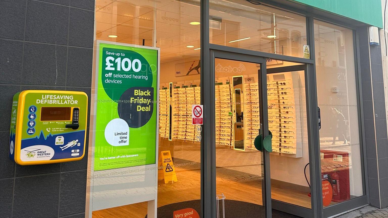 A defibrillator on the left front wall of a Specsavers branch.