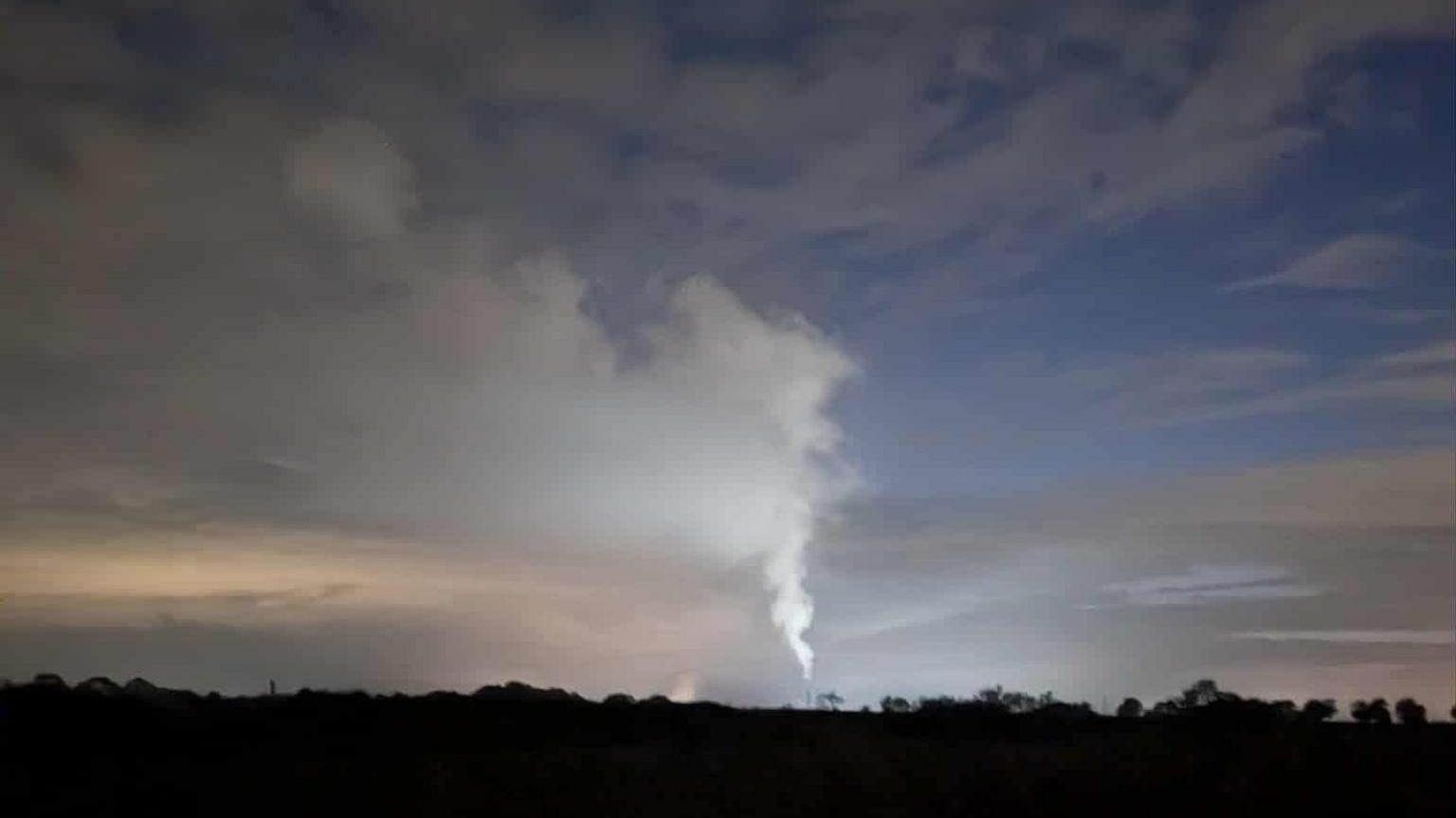 A night shot of steam rising in a rural setting. A white plume is rising up into the sky.