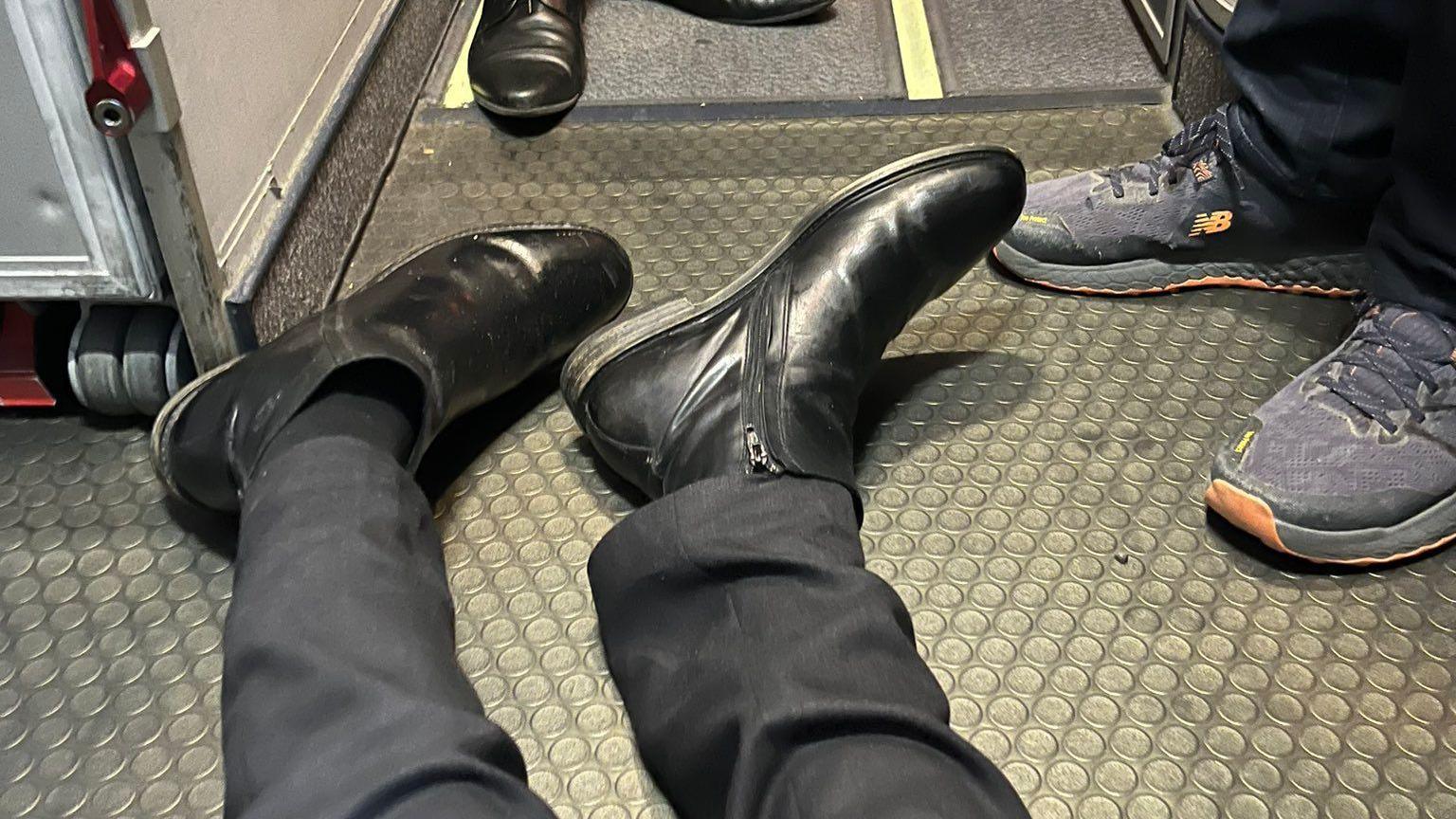 An image showing Frank Gardner's feet in a pair of black side-zipped boots, lying on the floor of the plane, clearly showing he is lying on the floor. Two other pairs of shoes are visible in the image. 