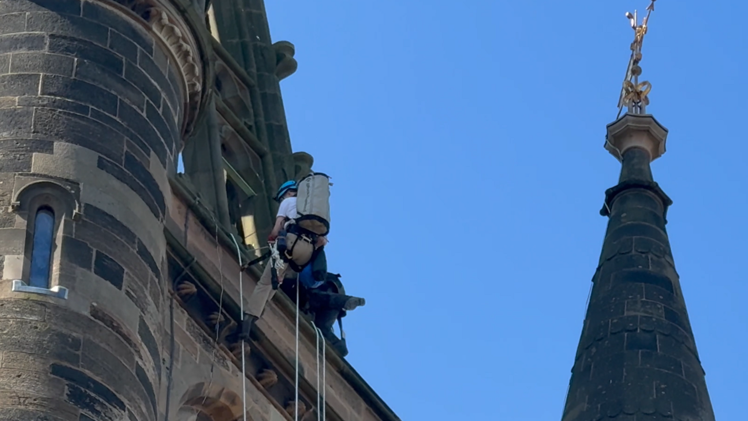 A man wearing a harness scales an old Gothic building tower