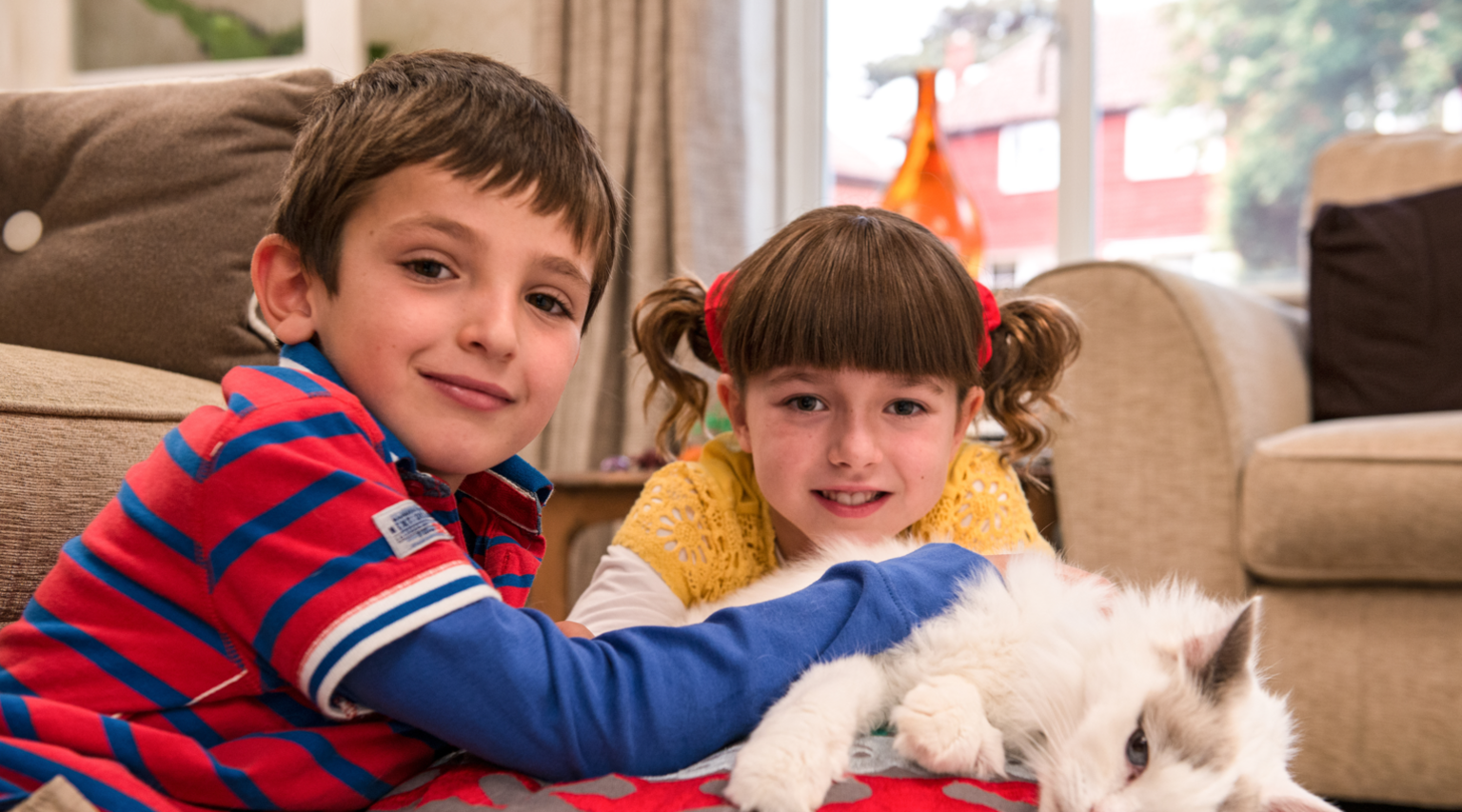 Two children smile while stroking a cat 