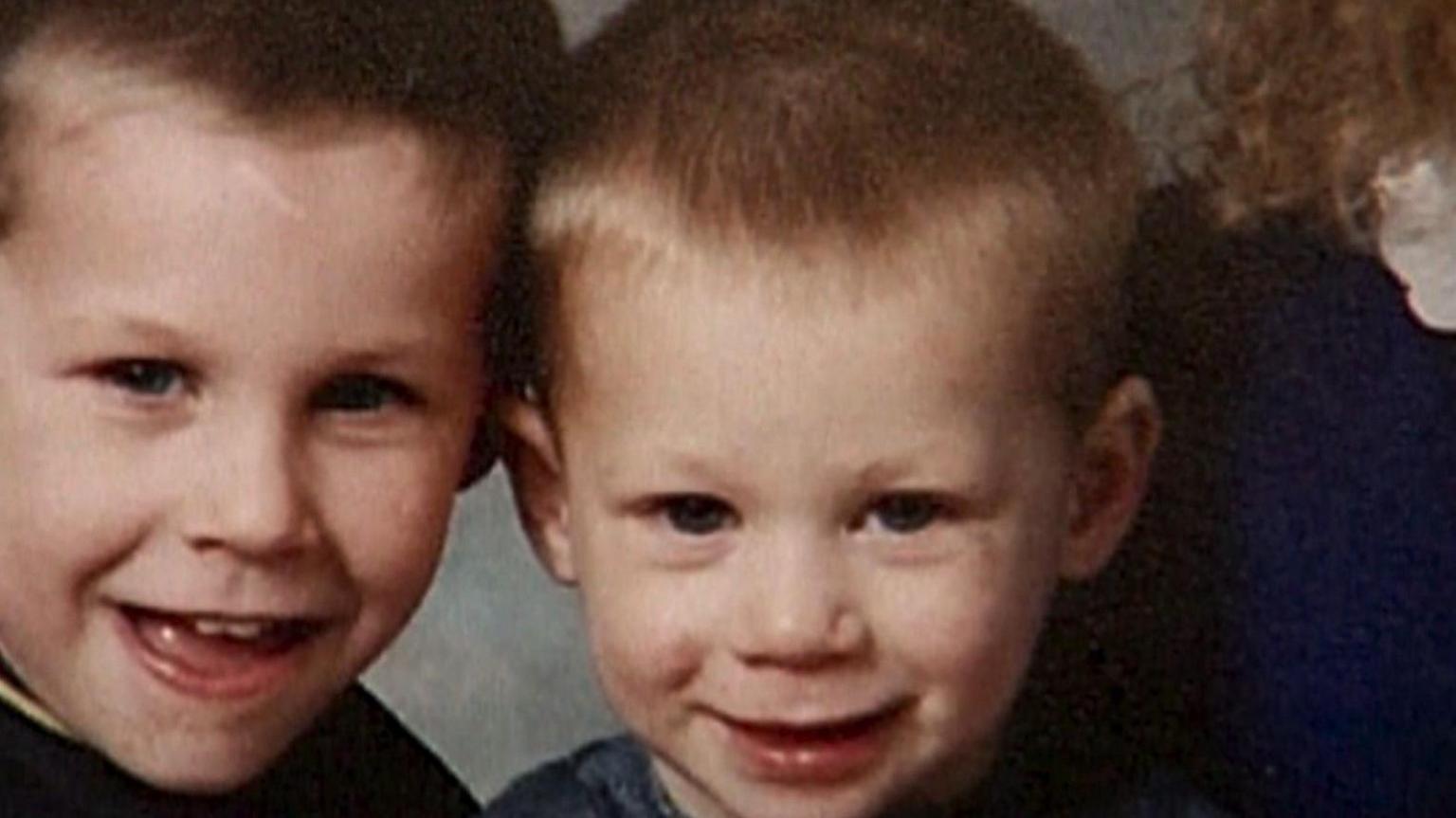 A 1990s picture of two young boys, aged around eight and six. They are both blond and smiling into the camera.