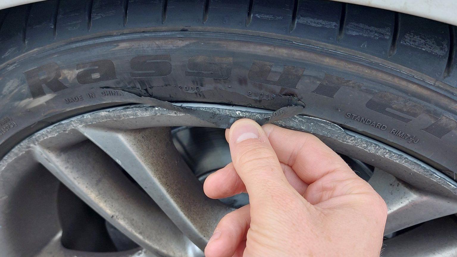 A man's hand is seen examining a car tyre which appears to have a partially split trim