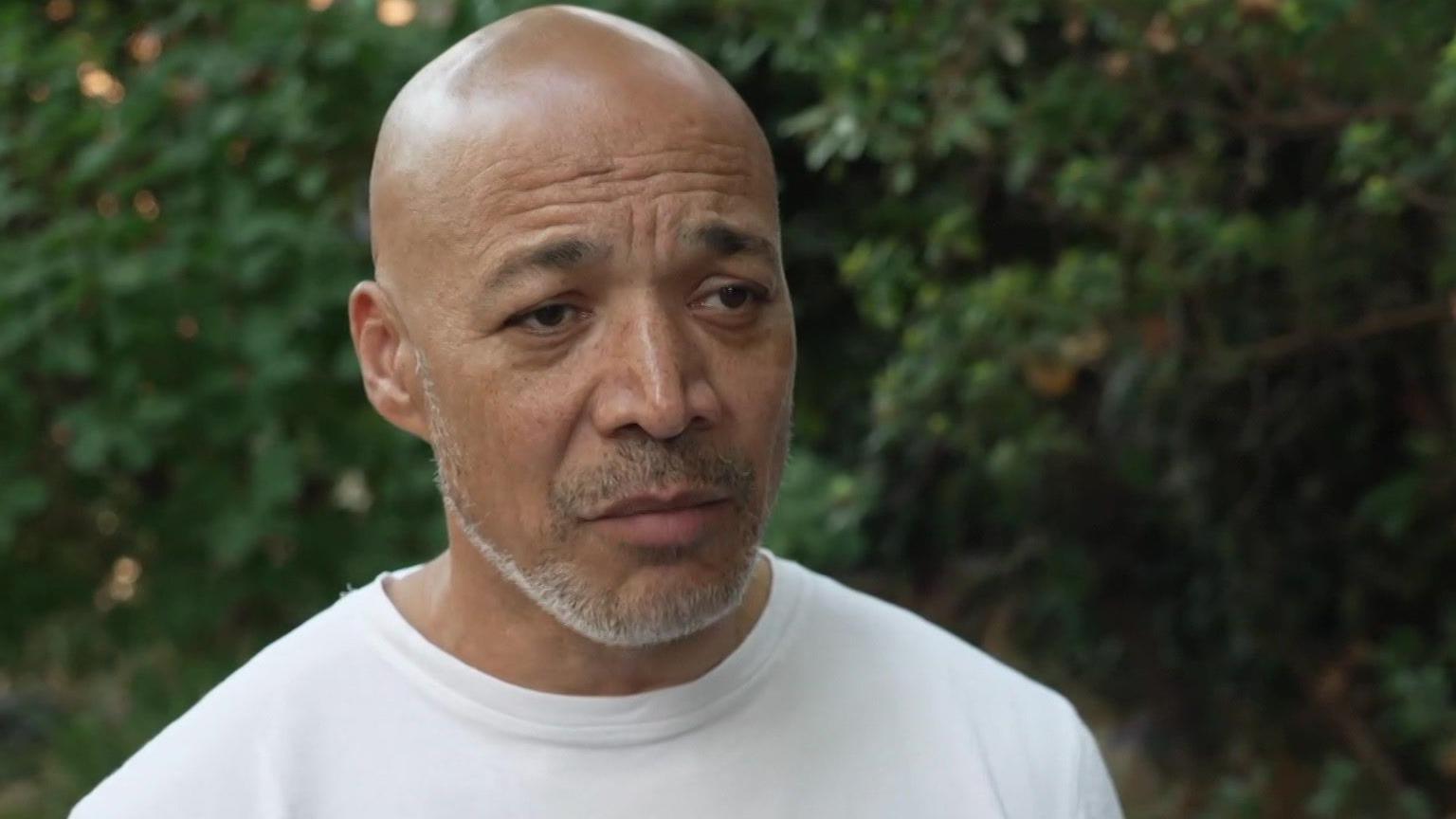 Matthew Phillip in a white t-shirt in front of greenery.