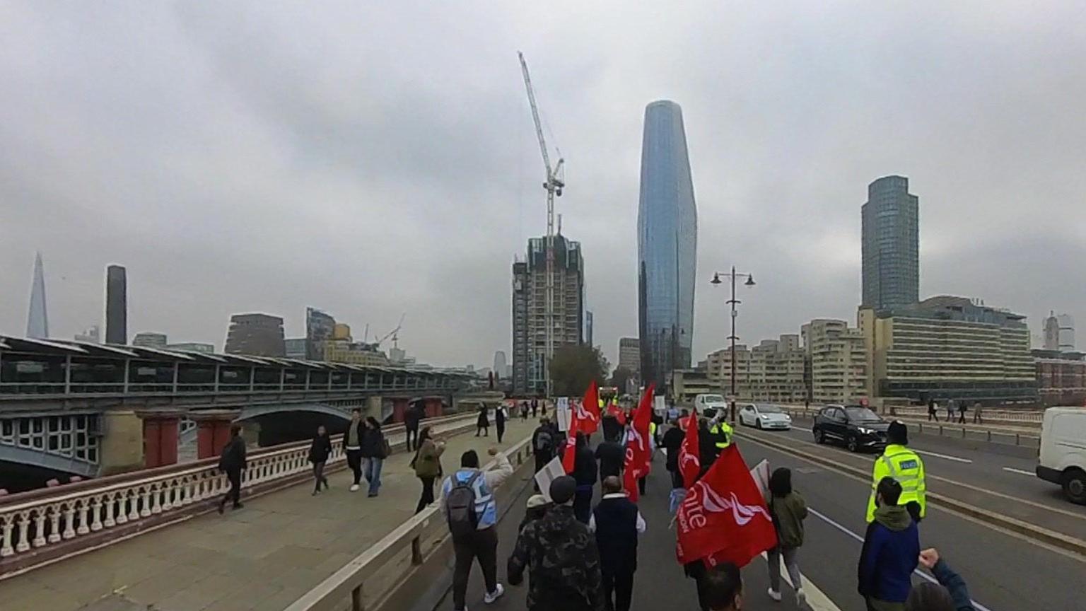 Image of people crossing a bridge in London. Some people are holding placards and flags.