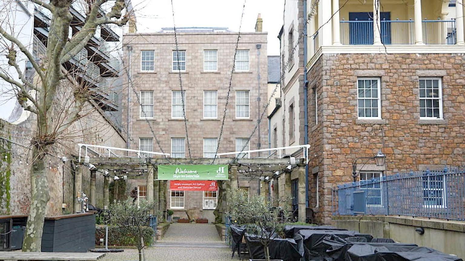 The Jersey Museum building with a large walkway and tables and chairs covered to the right on a grey skied day.