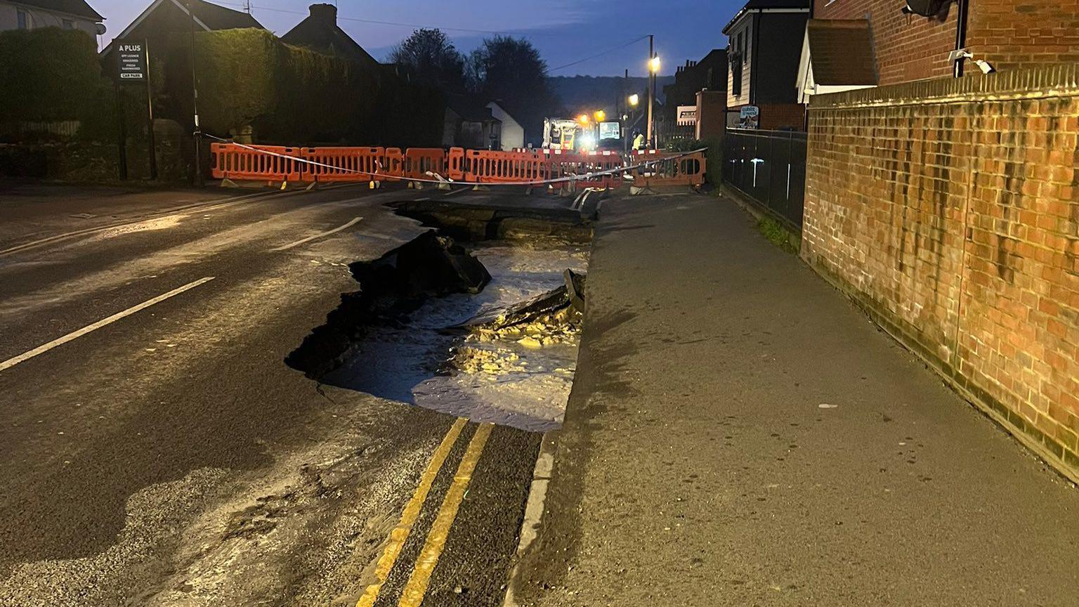 A night view of the sinkhole shortly after it first appeared. There is a pavement to the right, as well as a brick wall. 