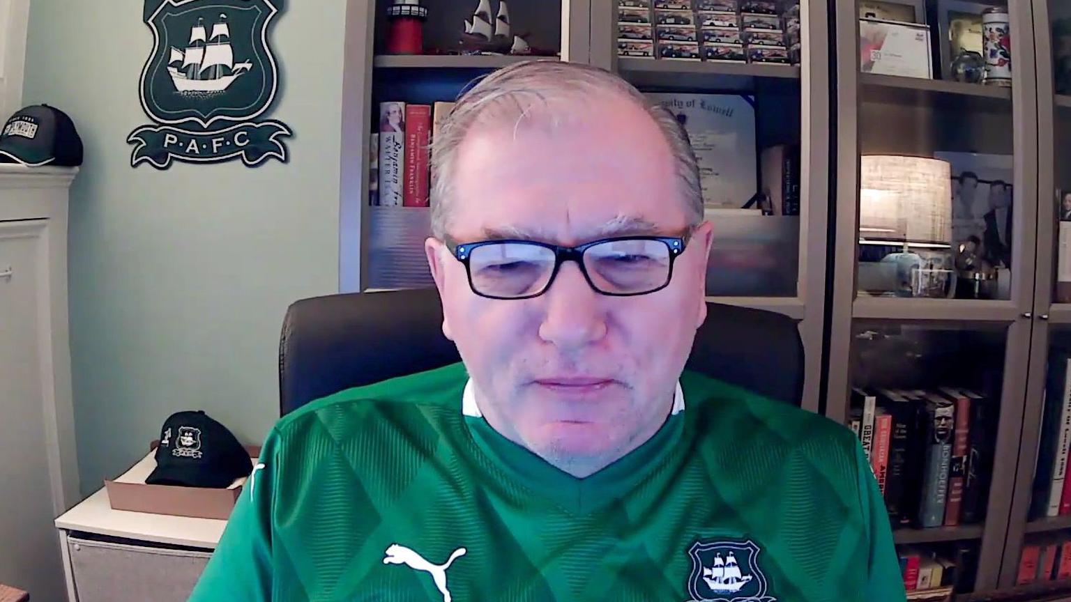 A man with glasses in a green football shirt.