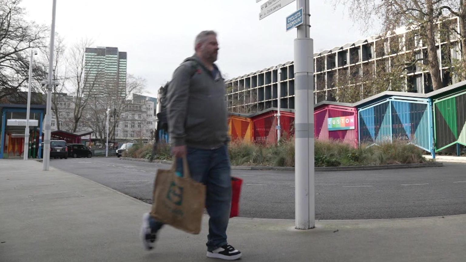 A man carrying bags walks past an empty cab rank