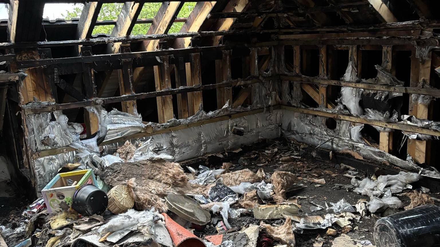 The gutted family home. All of the beams are charred. Burned items can be seen on the floor.