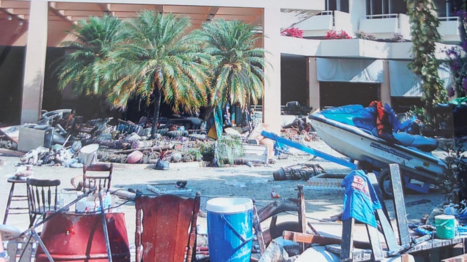 A street lined with buildings and palm trees which is filled with debris and a jet ski