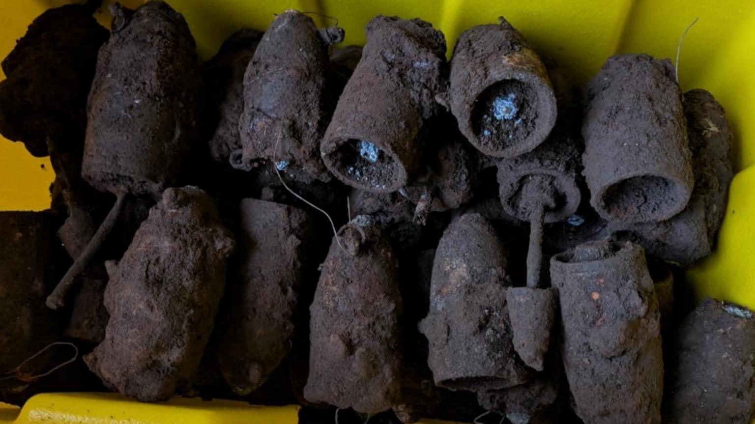 A pile of rusted and muddy bombs in a yellow box. They are shaped like bullets but larger.