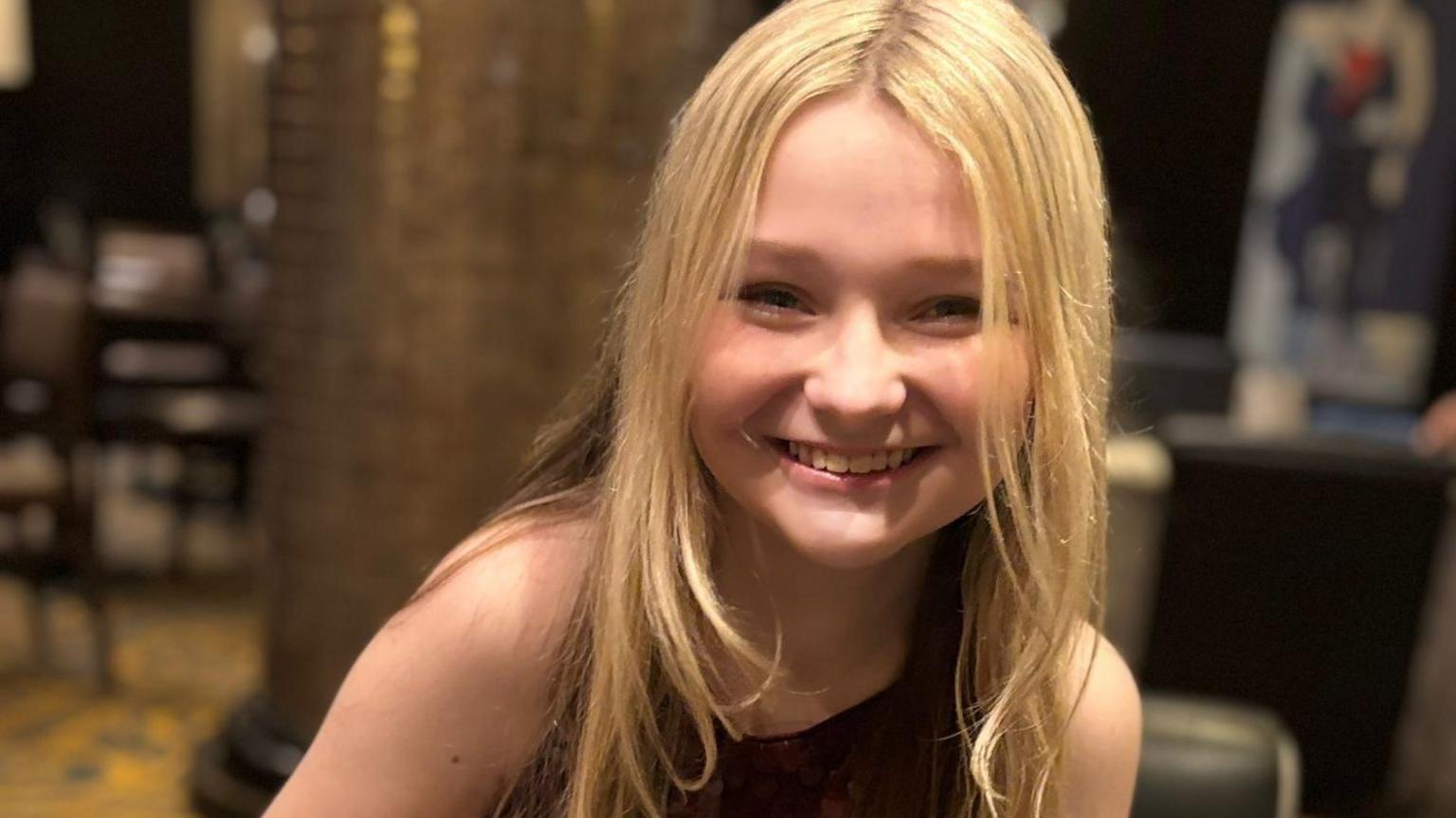 Isla, who has long blonde hair, smiles at the camera.