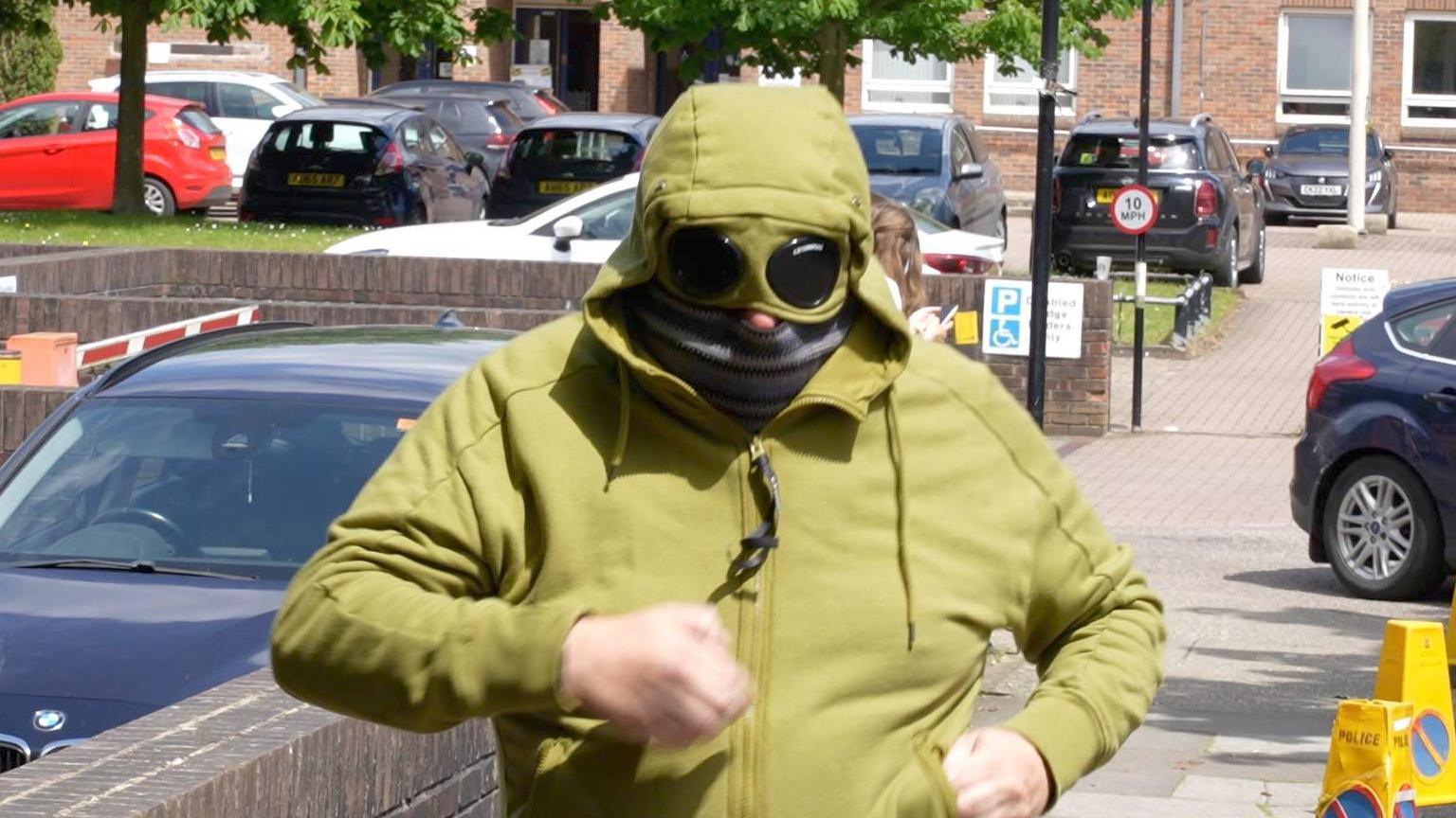 Man in green hoodie with attached goggles covering his eyes and a scarf over his face