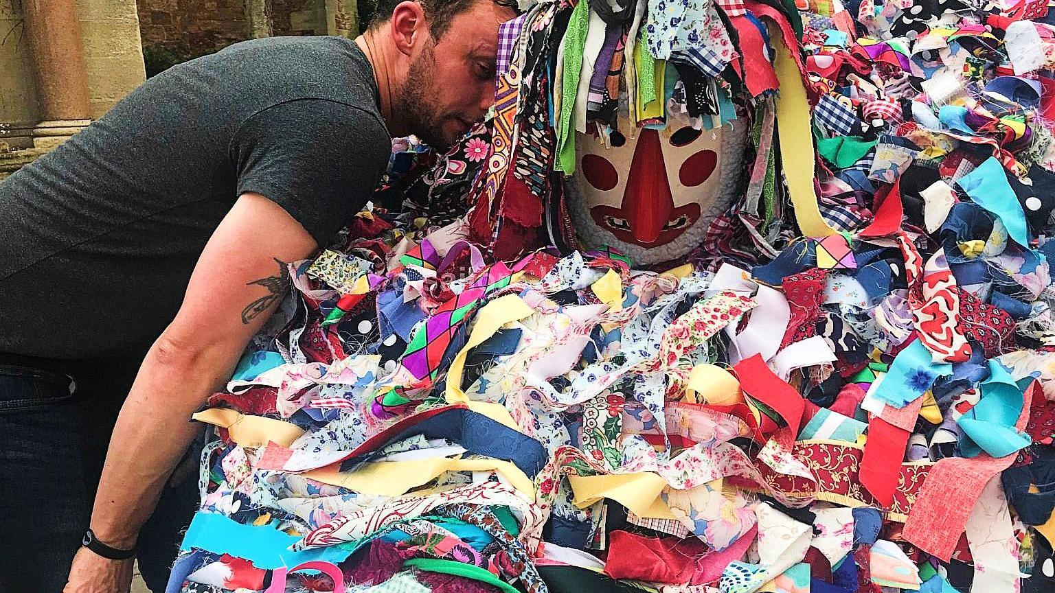 A man leans over to talk to another man, who is inside a hobby horse covered in colourful rags