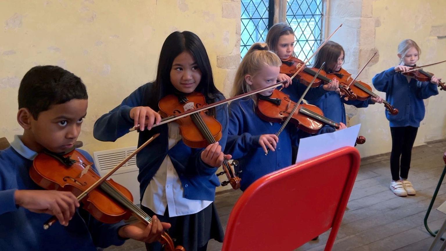 Five girls and a boy stood in a line playing violins. 