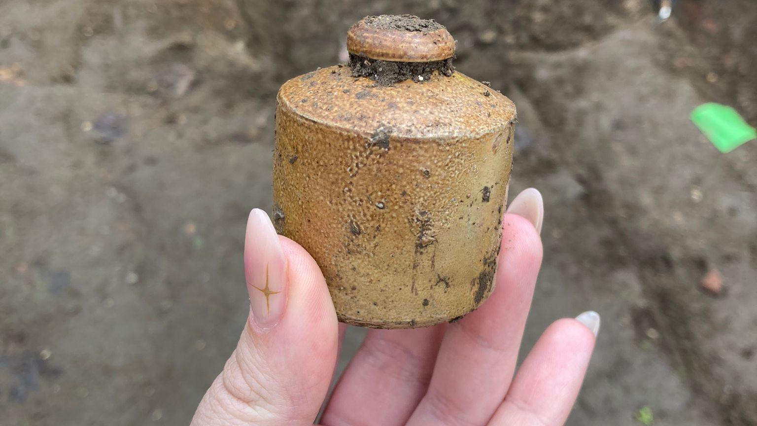 A woman's hand is in the picture holding an ancient pot that was discovered during an archaeological dig.