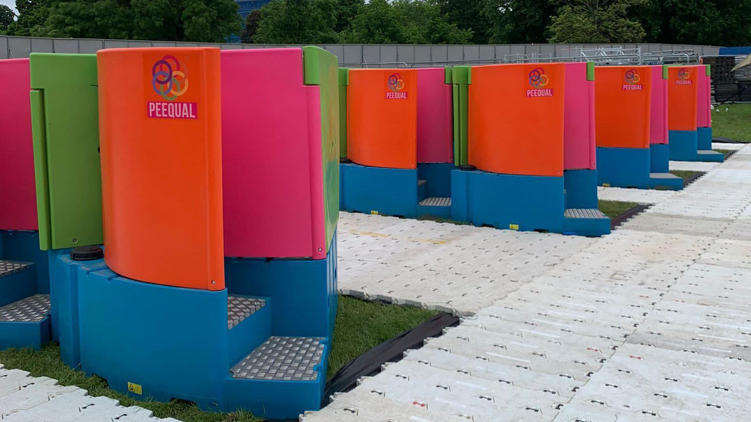 Several brightly-coloured PEEQUAL women's urinals on a festival site.