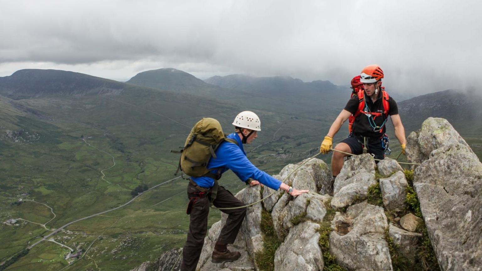 Two young people crest the summit of a mountain in Snowdonia