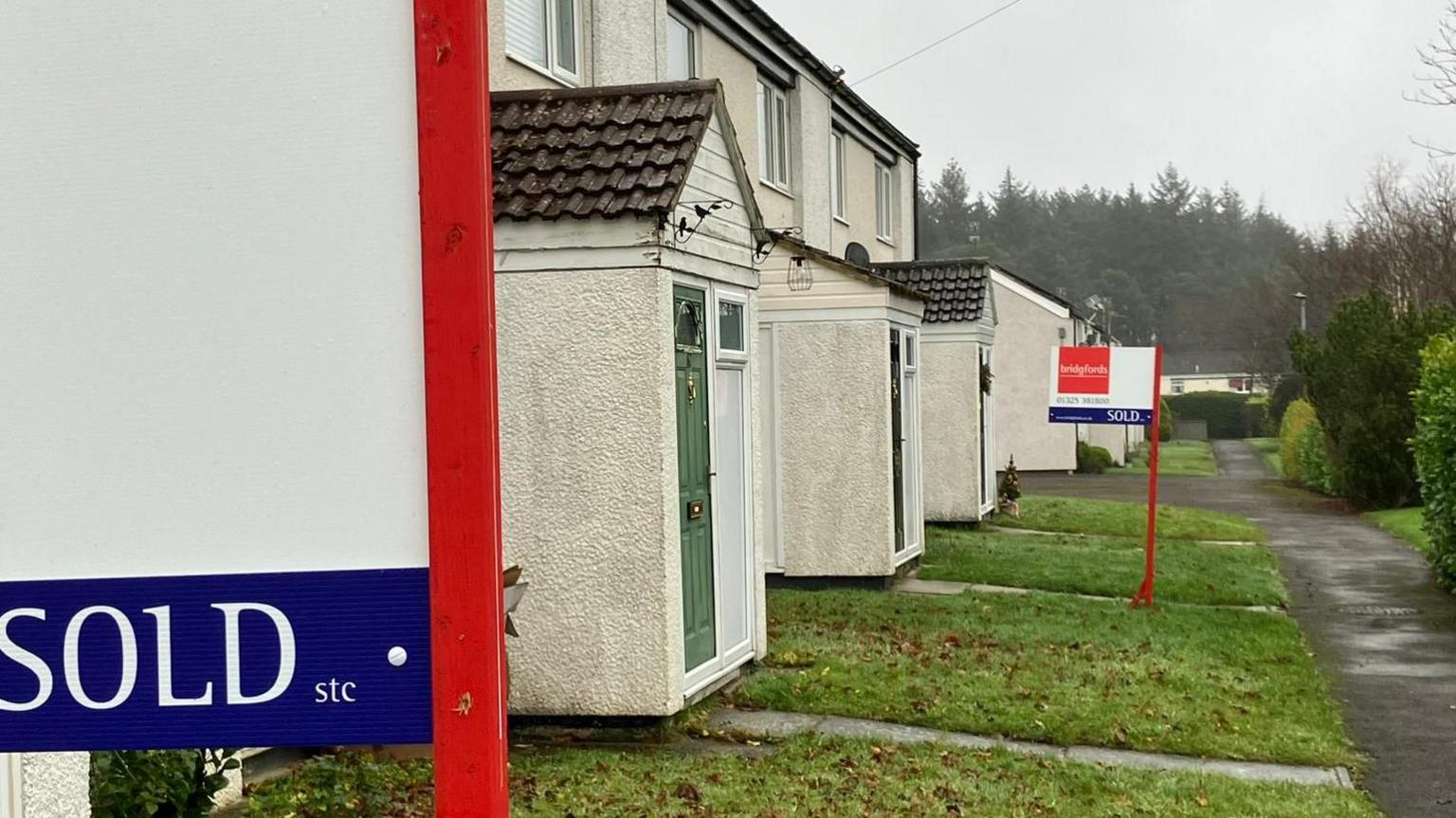 A row of former Army houses with "sold" signs out front. The day is grey and the scene gloomy.