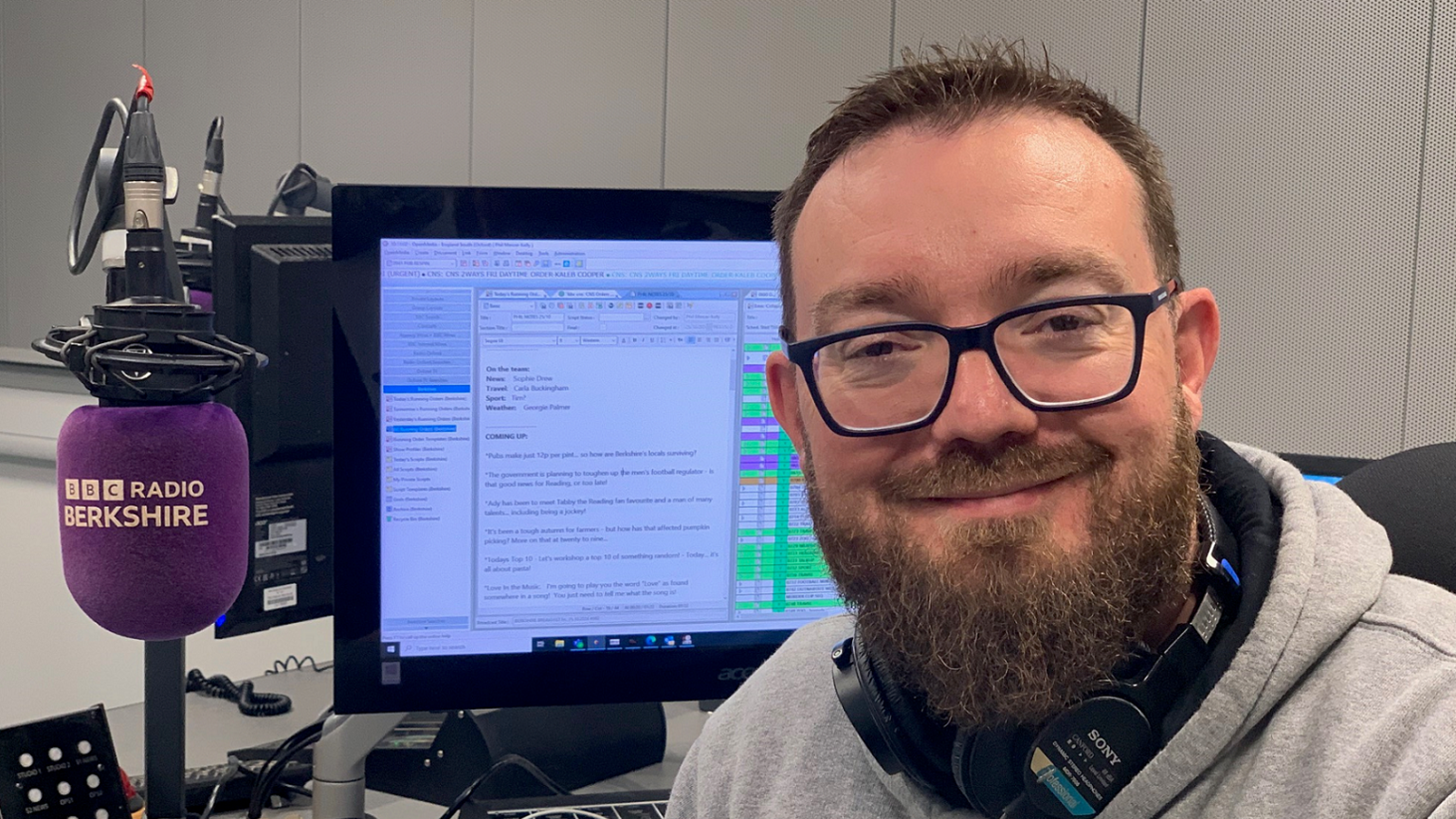 Phil Mercer sat in front of the BBC Radio Berkshire purple microphone in the station's studios. He has a beard and short hair and headphones around his neck