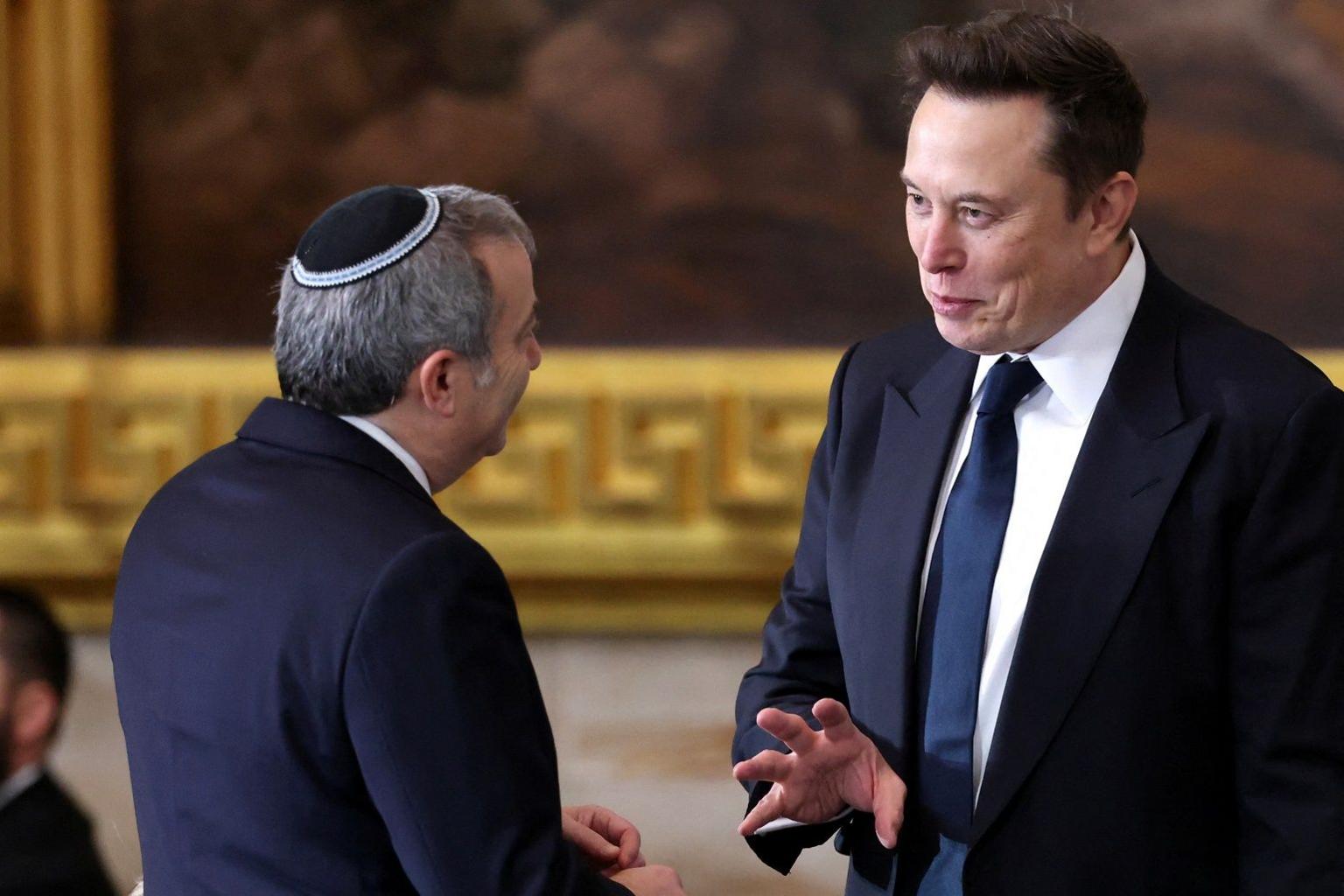 Elon Musk is seen speaking to a man wearing a kippah who is seen from behind - Musk appears to be making an animated point and gesturing with his hand 