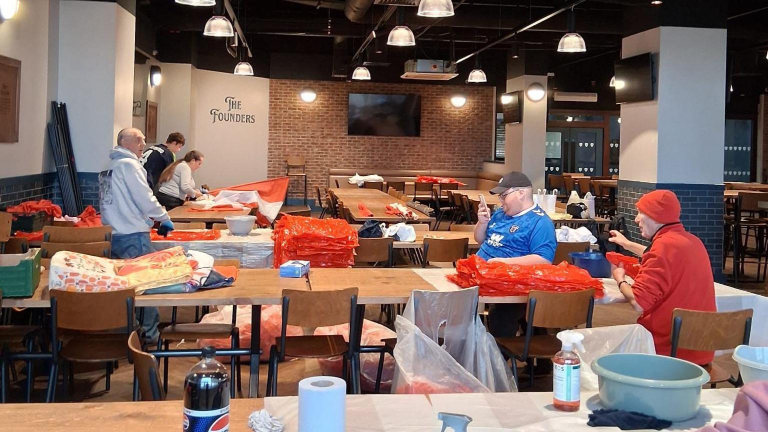 Squares of red and white plastic are strewn across tables with volunteers sorting and cleaning them.