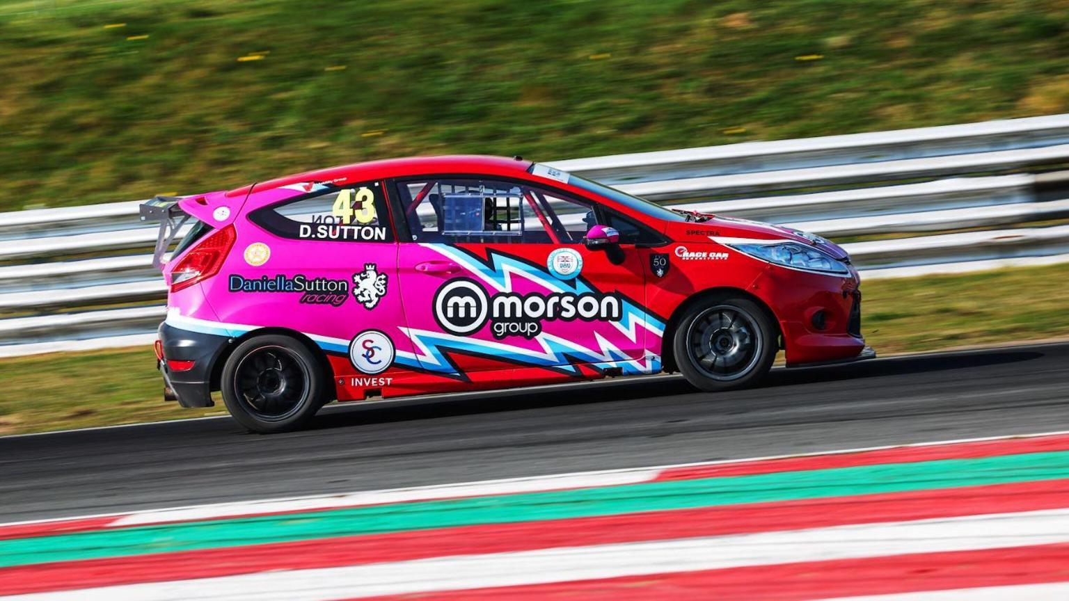 A Ford Fiesta with red and pink paint racing on a track.