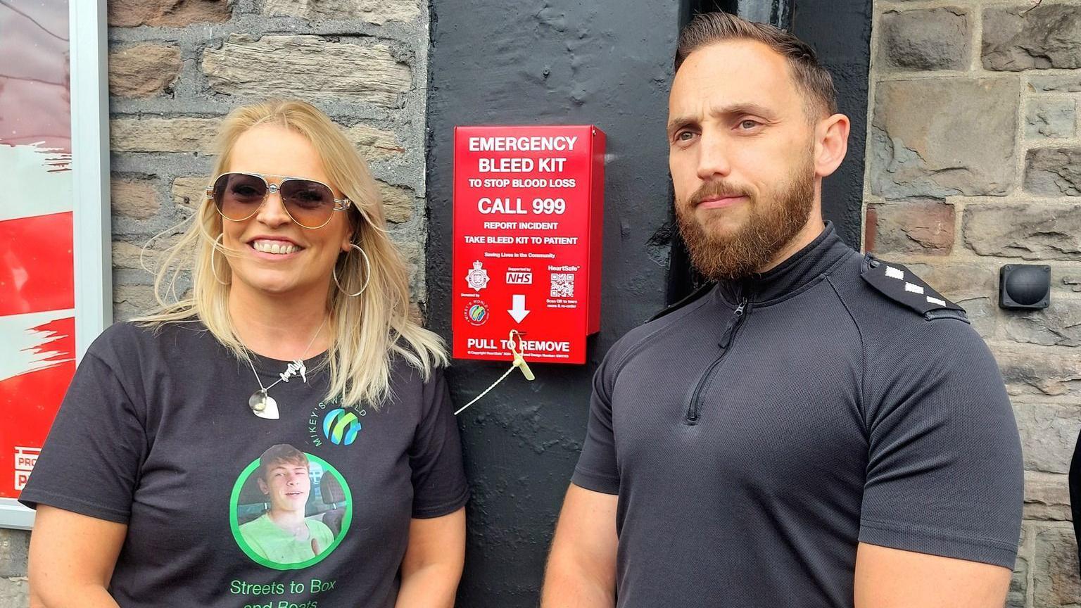 Hayley Ryall and Chief Inspector Mike Vass standing next to Mikey's World's first bleed kit outside The Cossham Inn