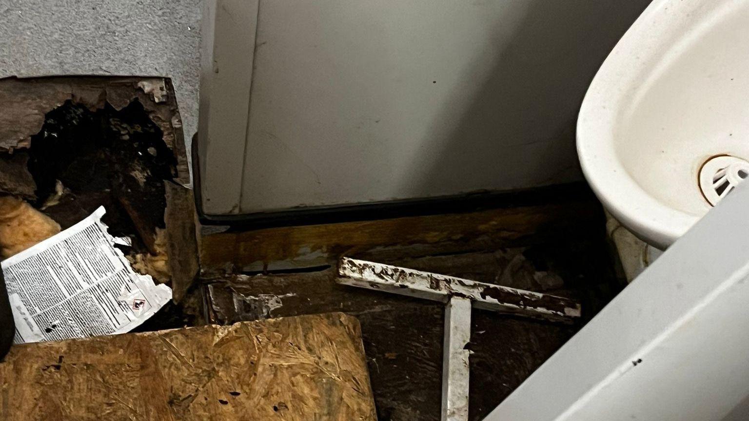 A rotten wooden fixture close to a urinal in a dingy bathroom. 