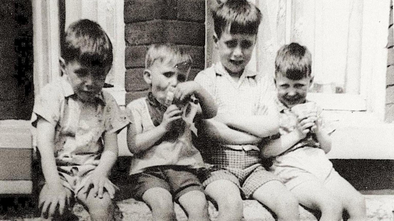 A black and white image of the four McGann brothers as children. They smile at the camera sitting on a stone wall.