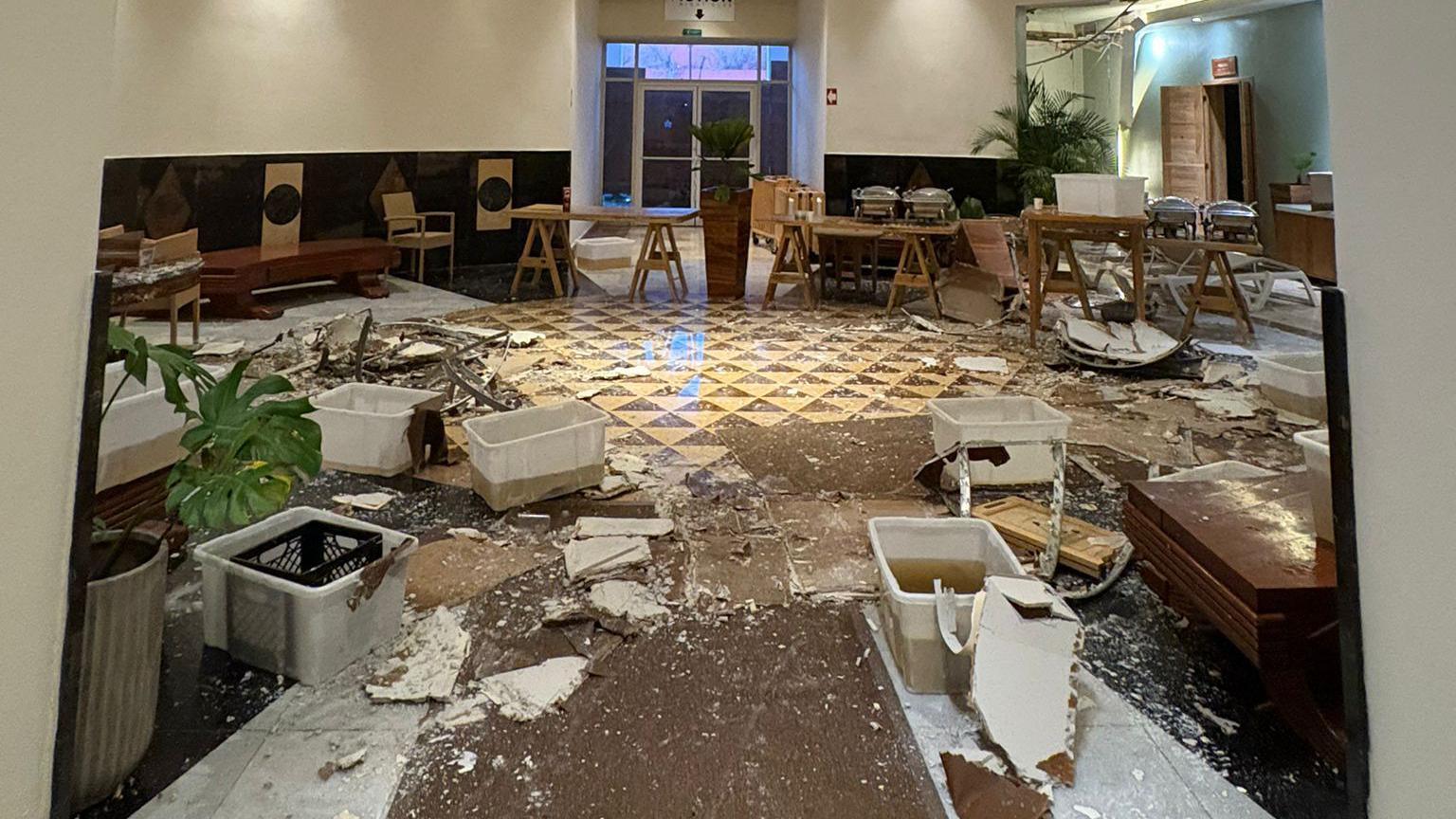 Broken pieces of ceiling plasterboad litters the floor of a reception space at the Iberostar Rose in Montego Bay. Buckets of dirty water at scattered arund the floor while tables and chairs are in disarray.