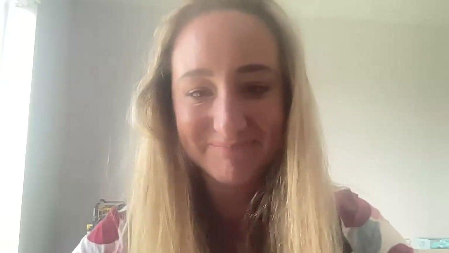 Screengrab from a zoom interview with a lady smiling into the camera, with long blonde hair, sat in front of a white wall.