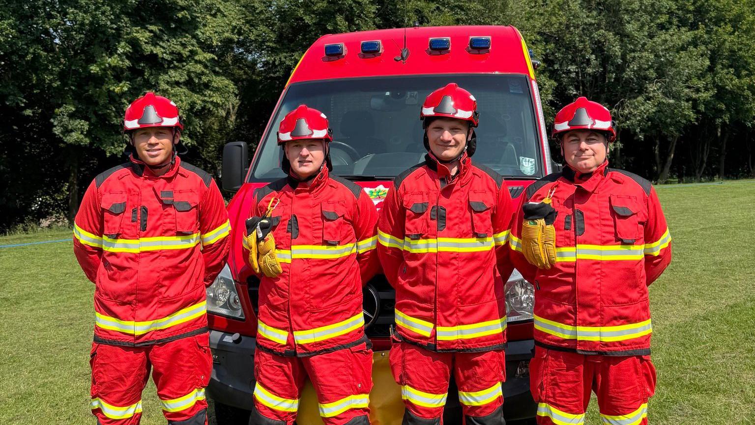 Four firefighters in red protective clothing in front of a new red wildfire support van.