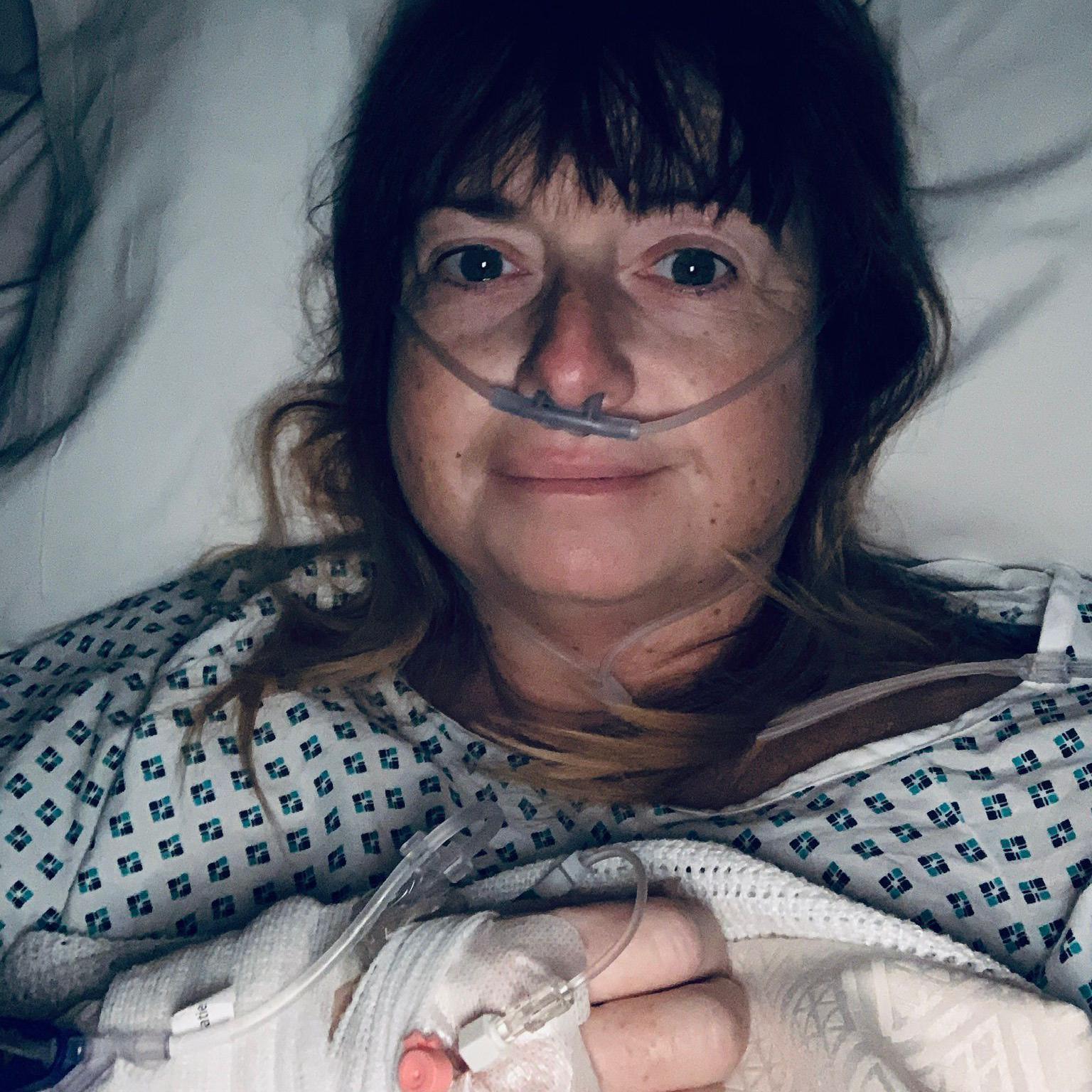 Selfie o Jo-Anne yn gorwedd ar wely ysbyty gyda offer anadlu yn ei thrwyn a drip yn mynd mewn i'w braich. 