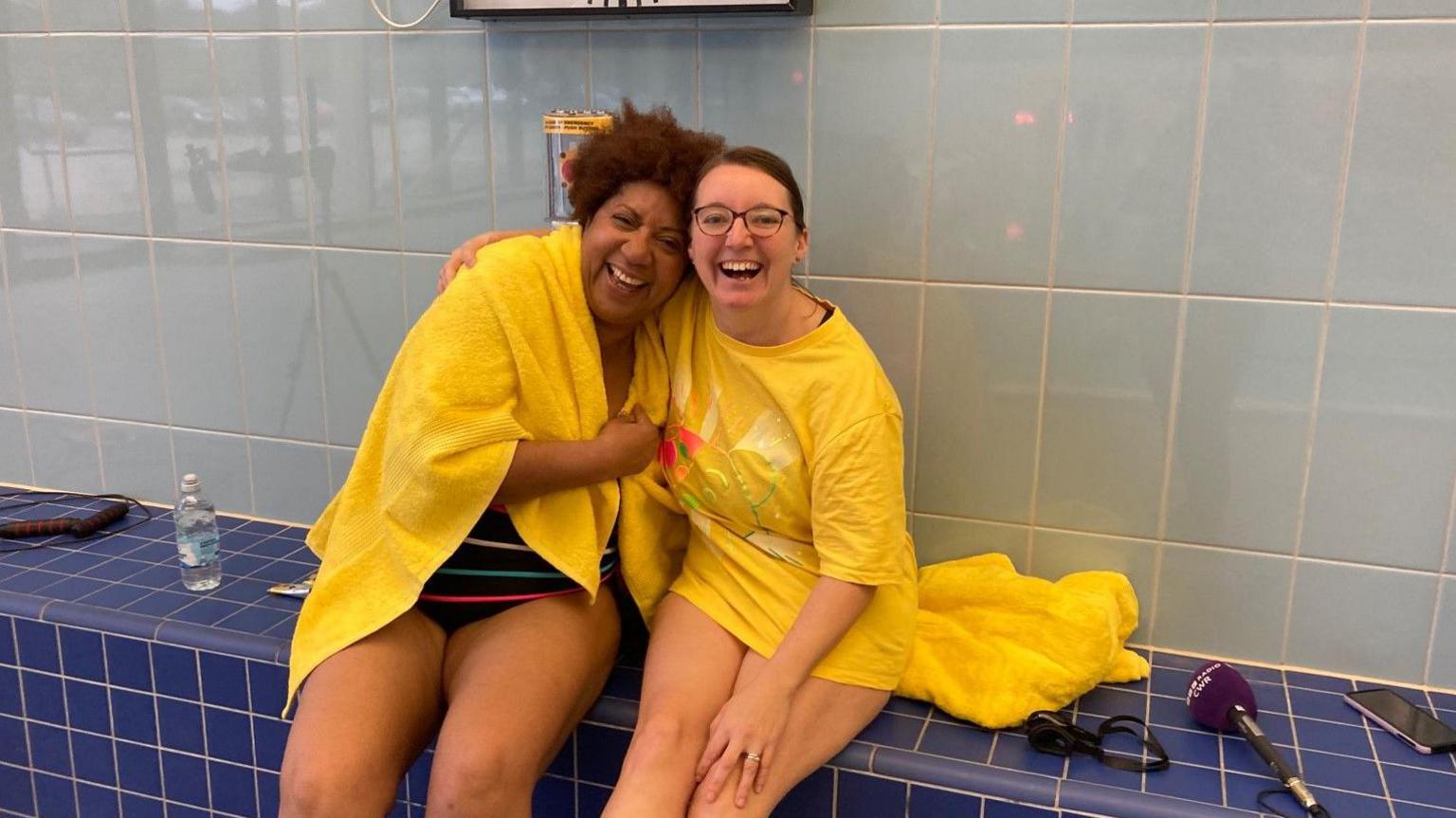 Debbie Woods' right arm is around Trish Adudu, who also has a towel around her, as they sit down on the opening day of the challenge