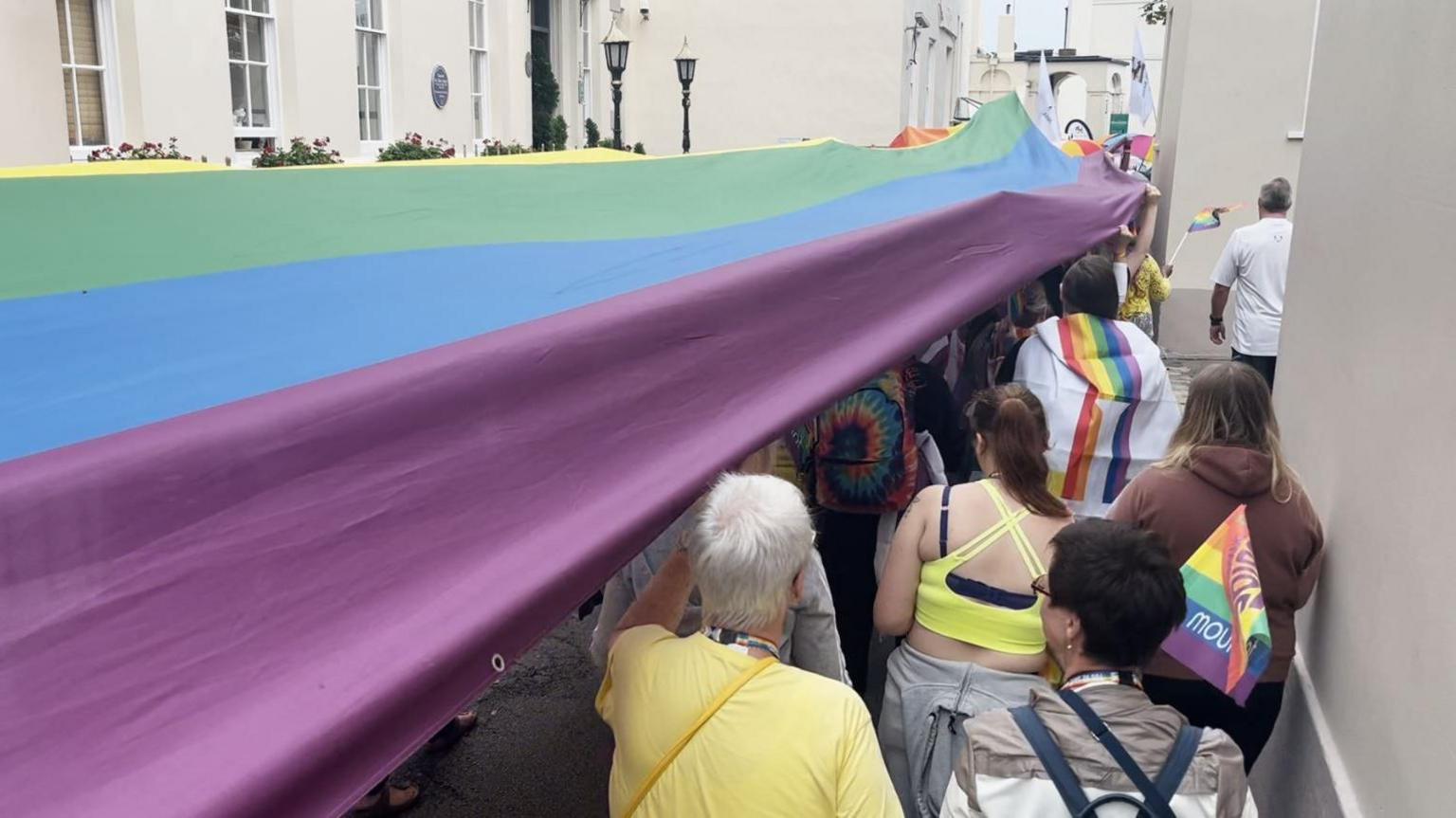 People walking in the parade holding a giant rainbow flag above their heads 