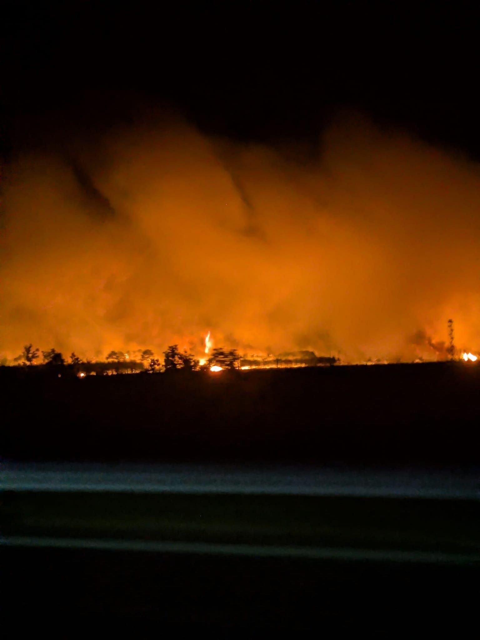 Flames are seeen next to the road illuminating the sky orange.