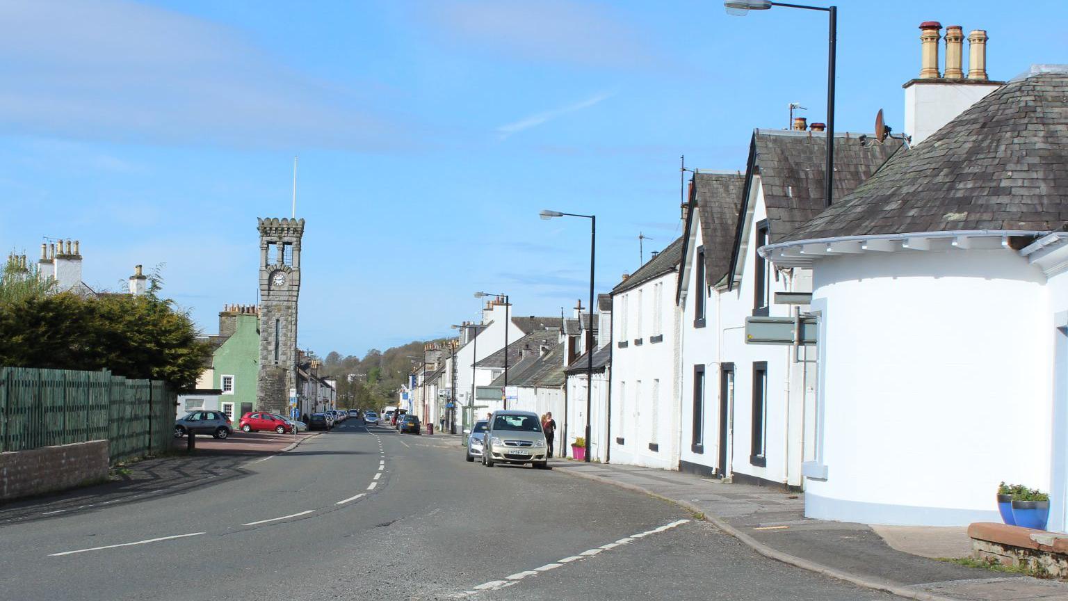The village of Gatehouse of Fleet with white houses down one side of the road and a large clock tower in the distance