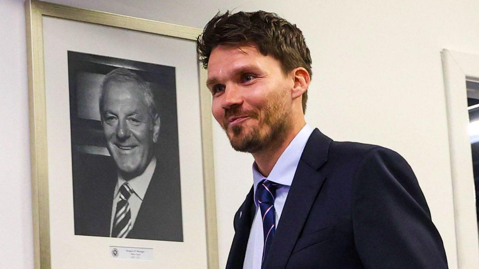 Danny Rohl walks past a picture of legendary former Rangers manager Walter Smith
