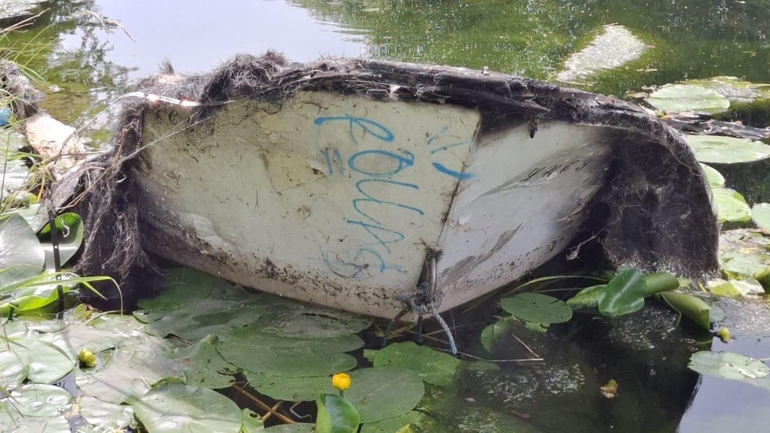 Rotted boat covered in moss upturned in canal